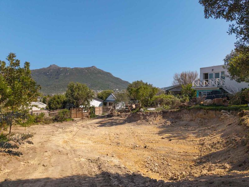 A vacant residential plot featuring excavated earth and a natural slope, offering mountain views and proximity to existing neighboring properties.