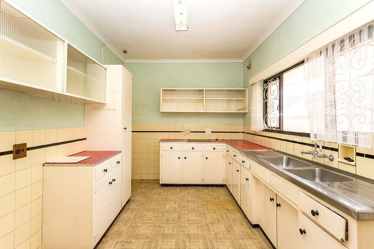A dated, empty kitchen featuring original cabinetry, double stainless steel sink, and tiled splashbacks, offering significant potential for a modern renovation.