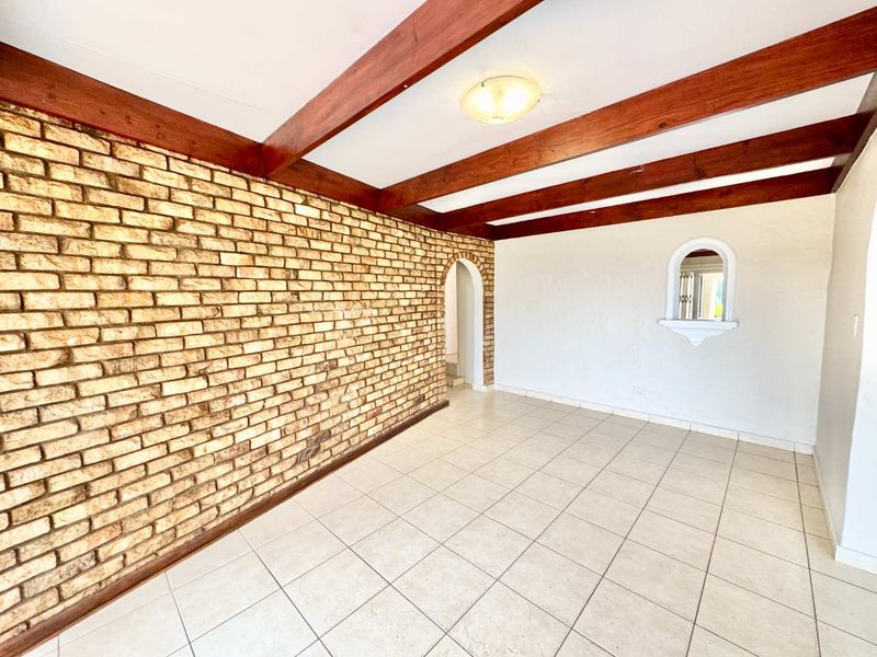 Spacious living area featuring a prominent exposed brick wall, timber ceiling beams, and neutral tiled flooring with an arched transition to adjacent spaces.