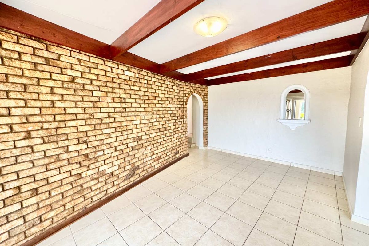 Spacious living area featuring a prominent exposed brick wall, timber ceiling beams, and neutral tiled flooring with an arched transition to adjacent spaces.