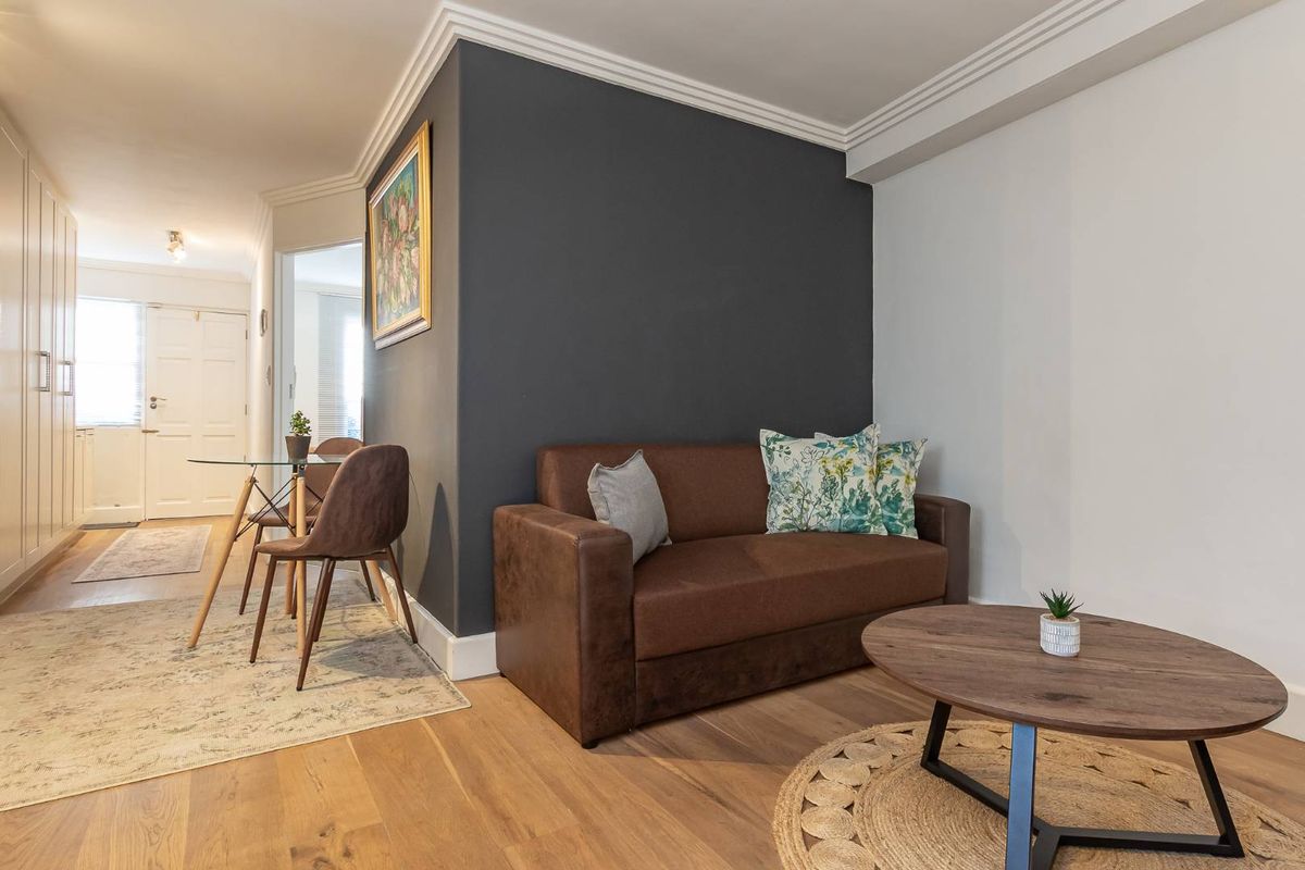 A well-maintained living area featuring light wood flooring, crown molding, and a dark accent wall, leading towards the apartment entrance.