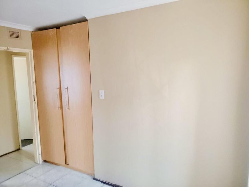 A simple bedroom featuring built-in wooden wardrobes, tiled flooring, and neutral wall tones, offering a blank canvas for personalization.