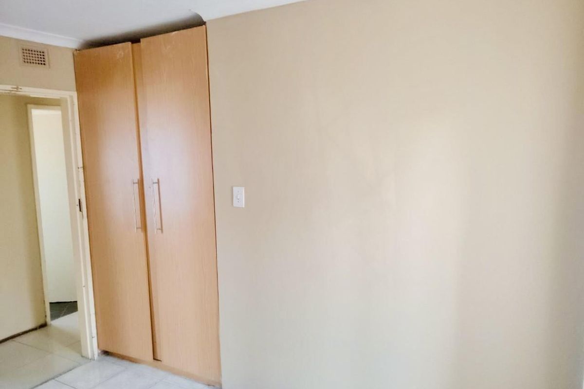 A simple bedroom featuring built-in wooden wardrobes, tiled flooring, and neutral wall tones, offering a blank canvas for personalization.