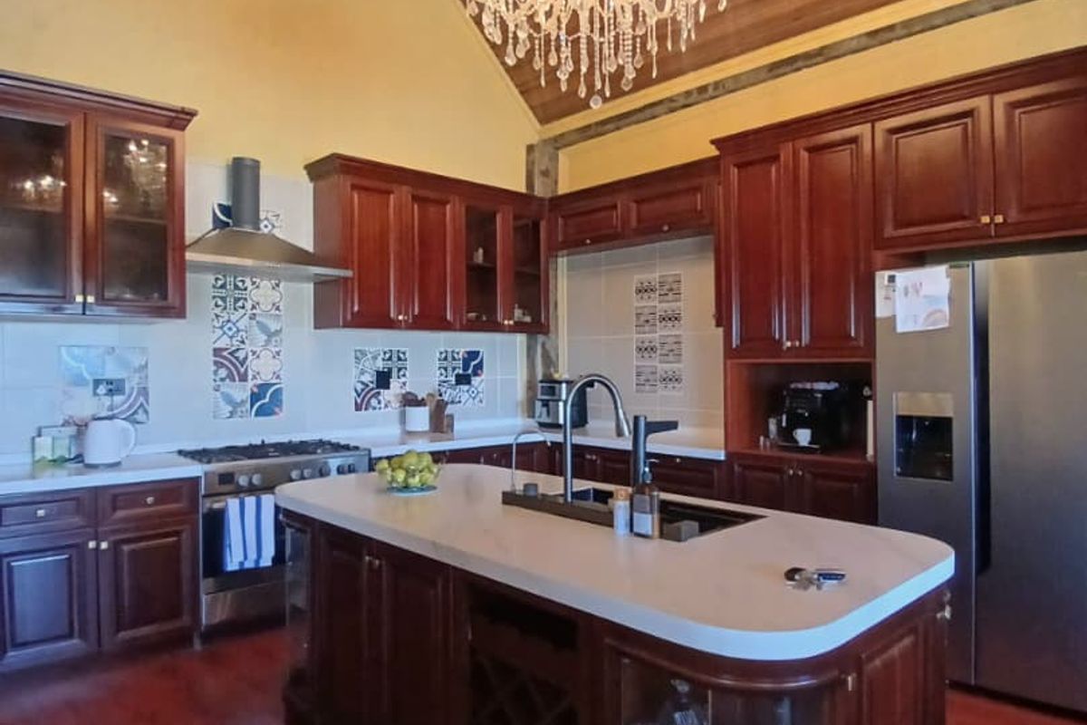 Spacious kitchen featuring dark wood cabinetry, a central island with stone countertops, a gas hob, and a vaulted ceiling with a decorative chandelier.