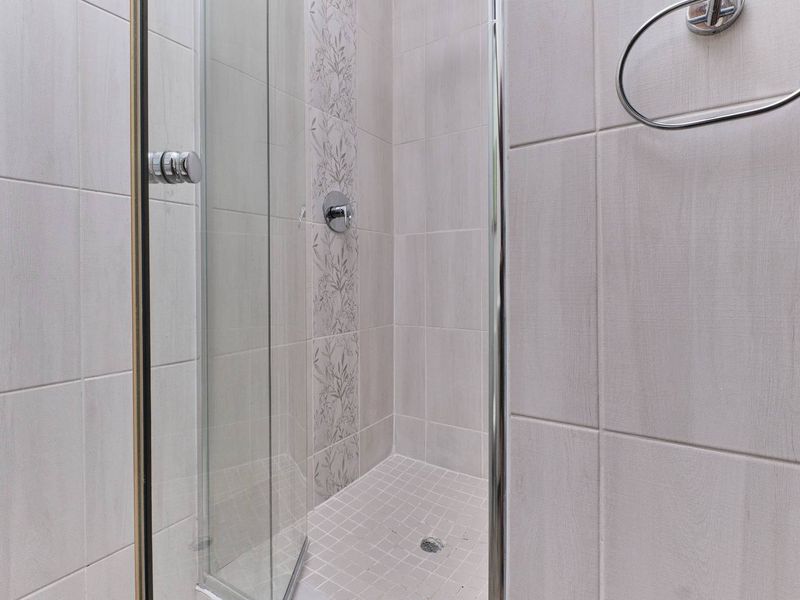 A clean, modern shower stall featuring neutral wall tiles, a decorative accent tile strip, and a glass enclosure.