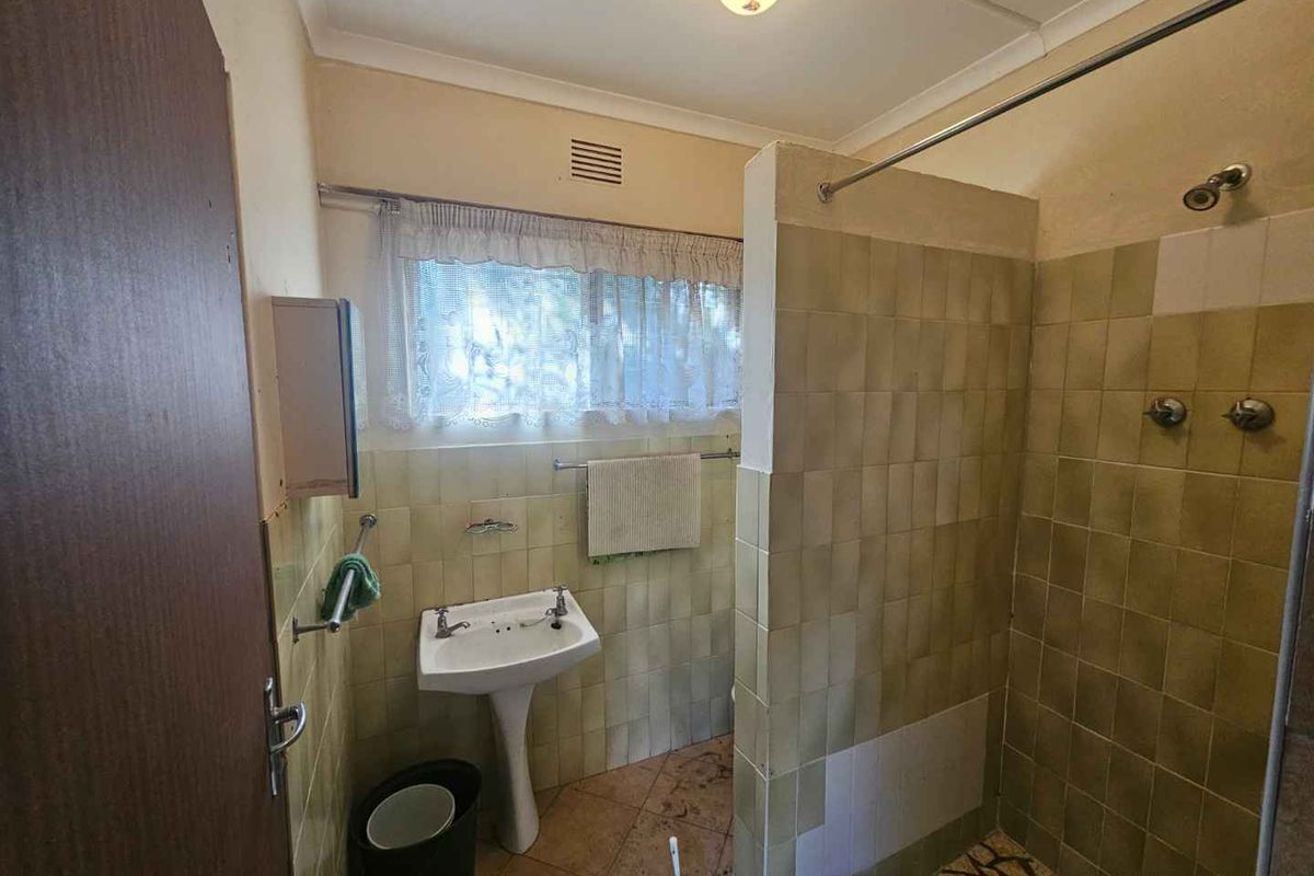A dated bathroom featuring a pedestal sink, a tiled shower enclosure, and original wall and floor finishes in need of modernization.