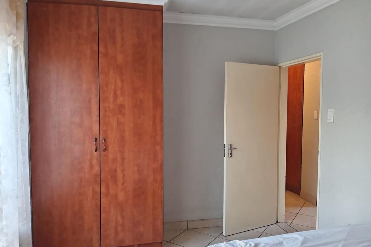 A bedroom featuring built-in wooden cabinetry, tiled flooring, and crown molding, providing a functional and neutral living space.