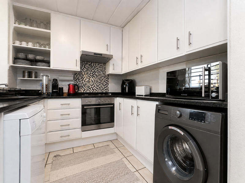 A functional kitchen featuring white cabinetry, black granite countertops, a mosaic tile backsplash, and built-in appliances including an oven and extractor fan.