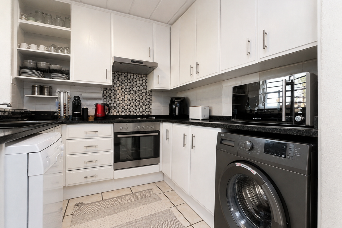A functional kitchen featuring white cabinetry, black granite countertops, a mosaic tile backsplash, and built-in appliances including an oven and extractor fan.