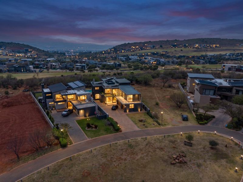 Aerial view of a modern luxury residence at dusk, featuring a paved driveway, multi-car garage, swimming pool, and expansive estate views.