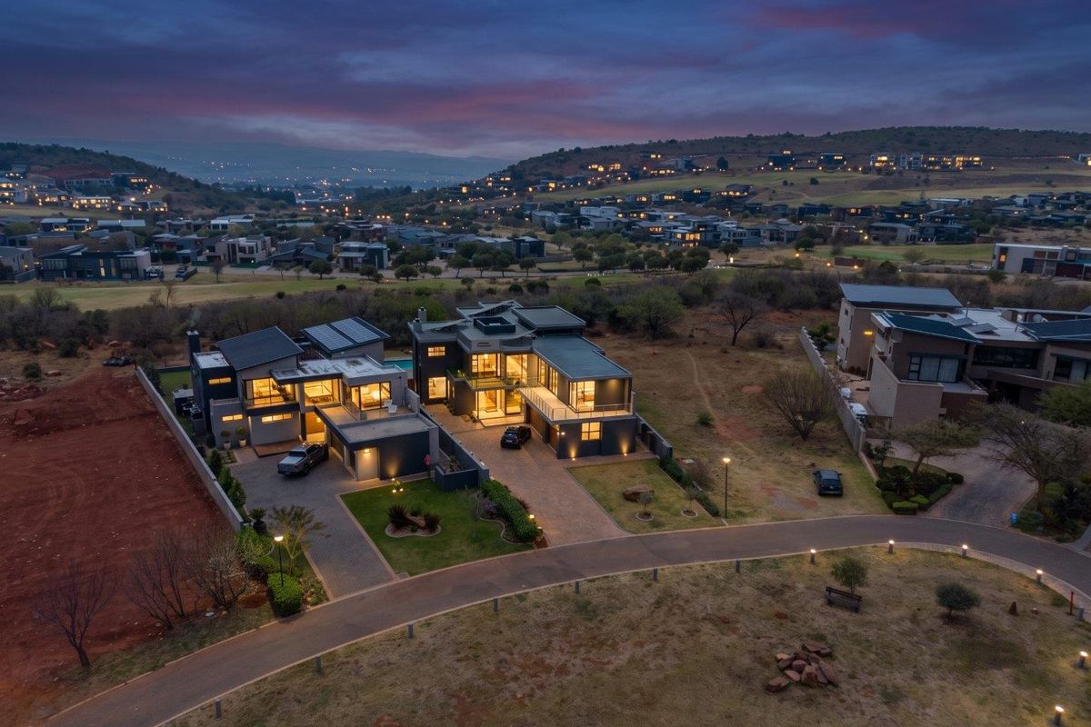 Aerial view of a modern luxury residence at dusk, featuring a paved driveway, multi-car garage, swimming pool, and expansive estate views.