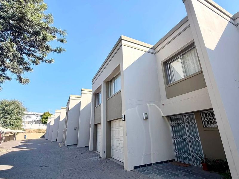 Front elevation of a townhouse complex featuring paved driveway access, individual garages, and secure entrance points with security gates.