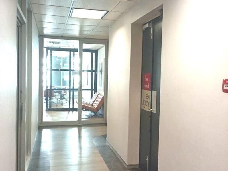 A functional office hallway featuring a suspended ceiling, recessed lighting, and a designated fire exit door with clear signage.