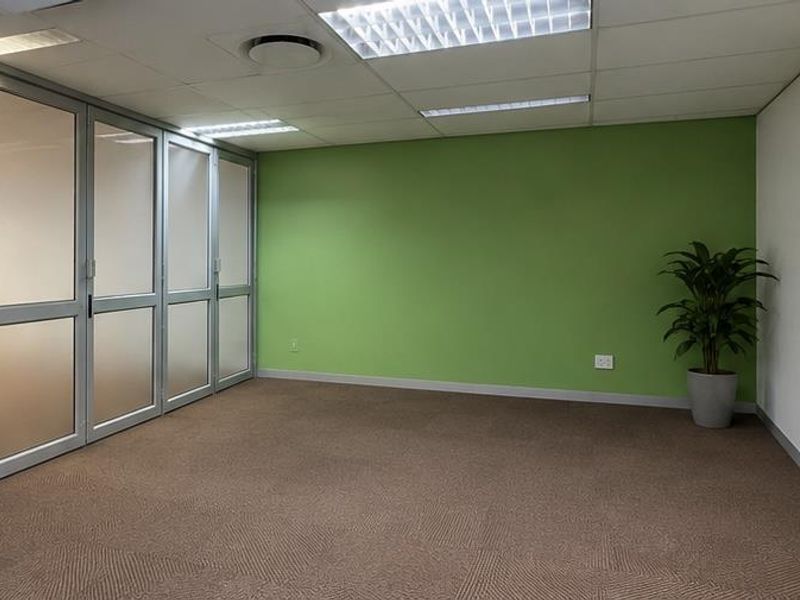 A clean, professional office space featuring frosted glass partitions, carpeted flooring, and a wall-mounted whiteboard, offering a bright and functional work environment.
