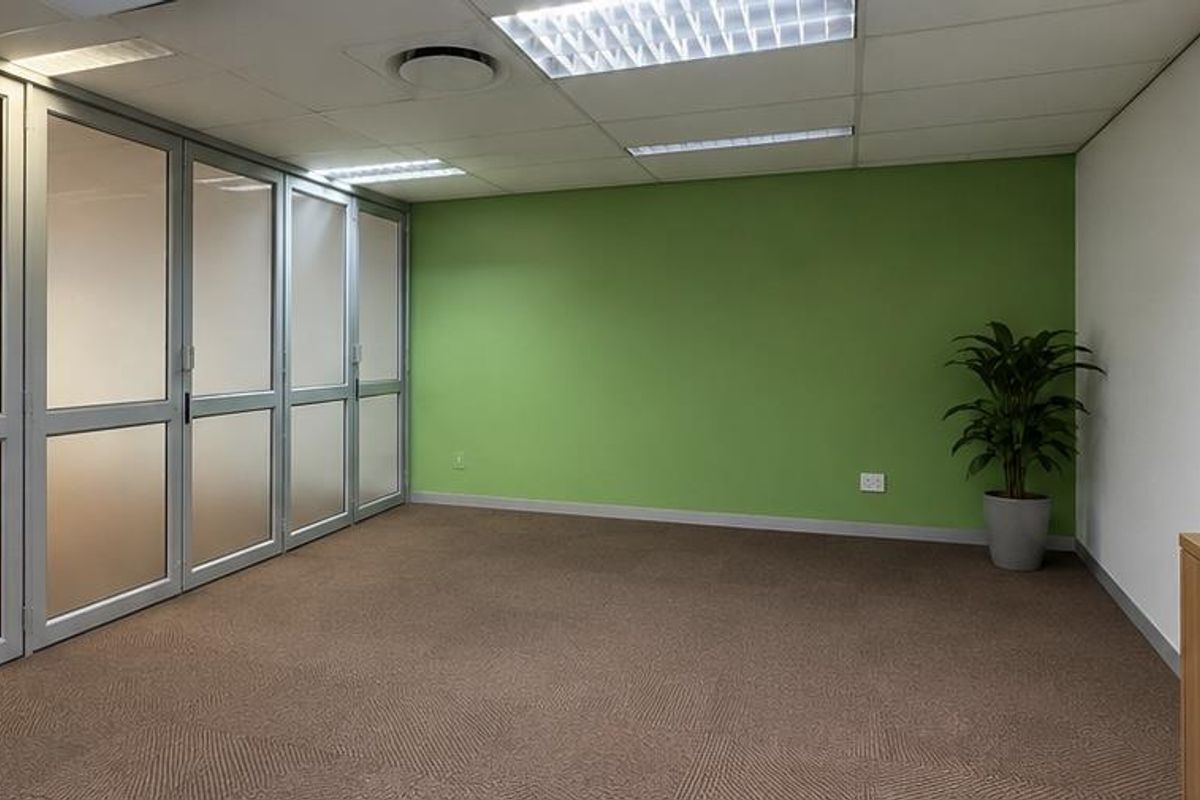 A clean, professional office space featuring frosted glass partitions, carpeted flooring, and a wall-mounted whiteboard, offering a bright and functional work environment.