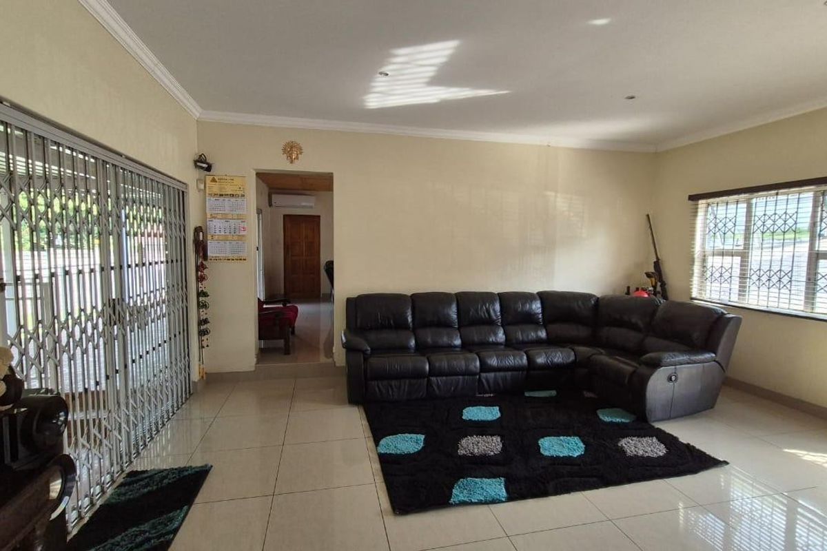 A spacious living room featuring tiled flooring, large windows with security bars, and a sliding door with a metal security gate.