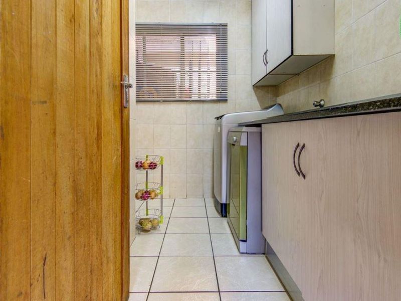 A functional laundry room featuring tiled walls and flooring, built-in cabinetry with a laminate countertop, and a window with fitted blinds.