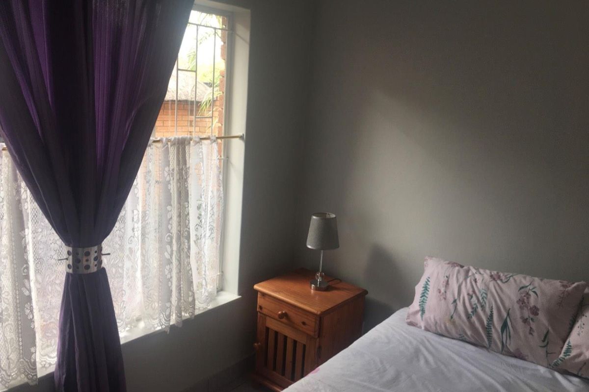 A bedroom featuring a window with security bars and tiled flooring.