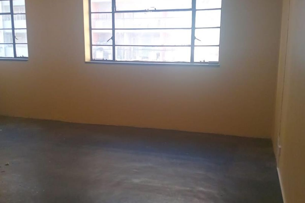 An empty bedroom featuring steel-framed windows and concrete flooring, offering a blank canvas for renovation and interior design updates.