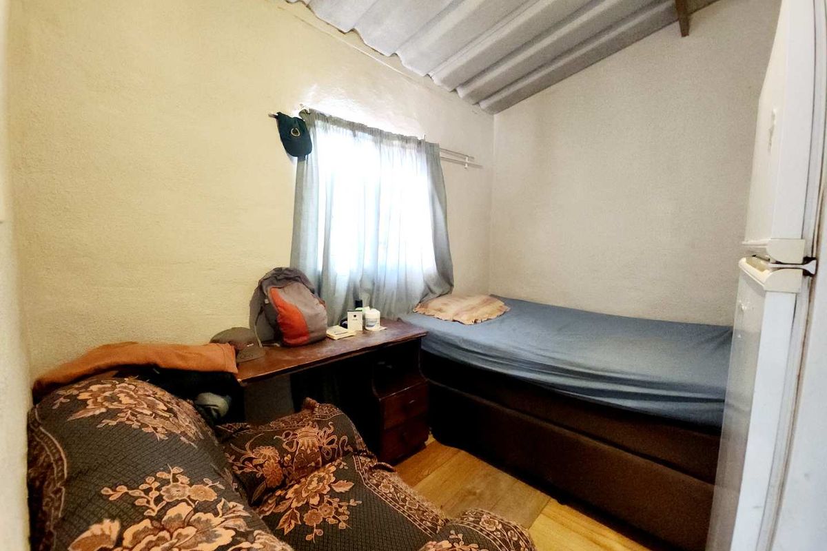 A compact bedroom featuring a single bed, wood-look flooring, and exposed corrugated ceiling panels.