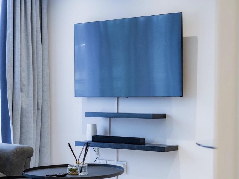 A modern living room wall featuring minimalist floating shelves and a wall-mounted television setup.