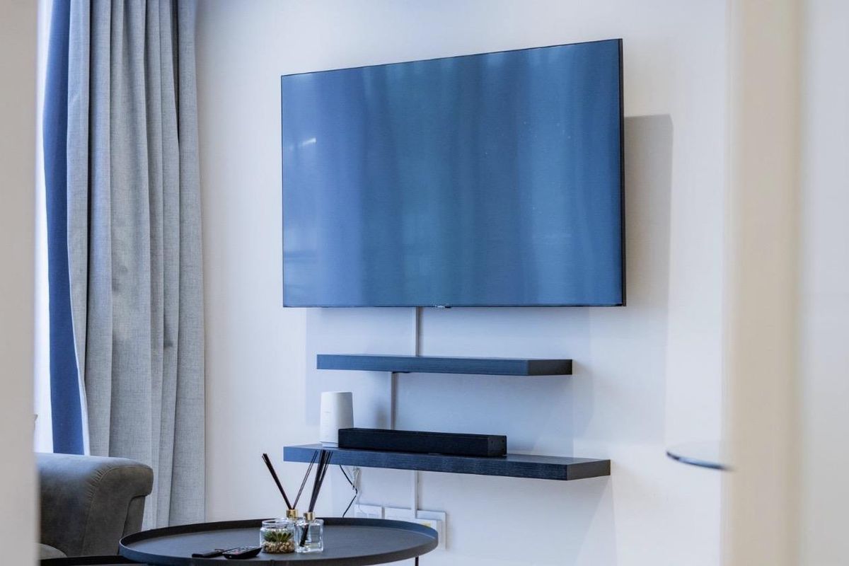 A modern living room wall featuring minimalist floating shelves and a wall-mounted television setup.