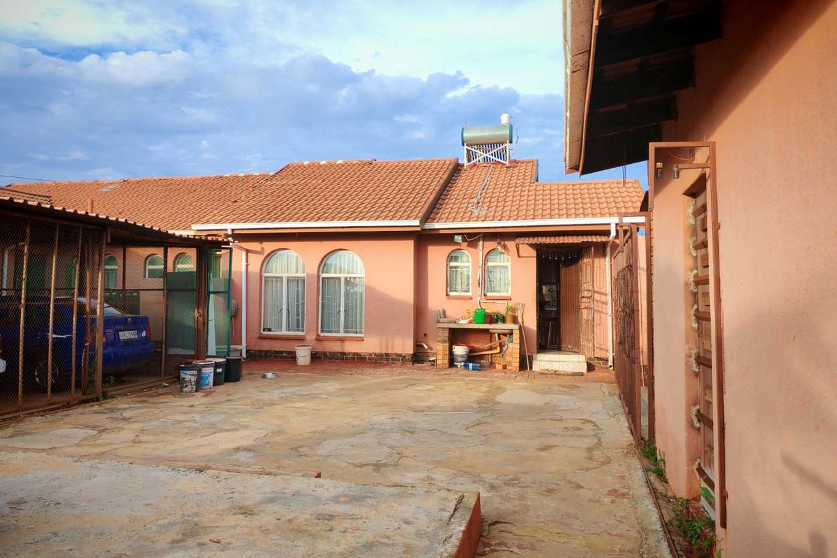 Rear exterior view of the house featuring a paved courtyard, arched windows, and a solar water heating system mounted on the tiled roof.