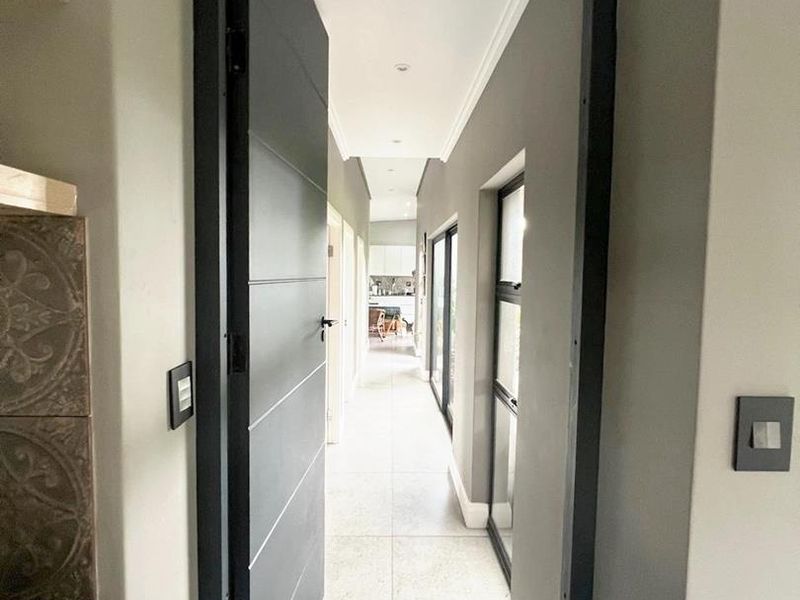 A modern, well-lit hallway featuring large format floor tiles, clean grey walls, and a contemporary door frame leading to an open-plan living area.