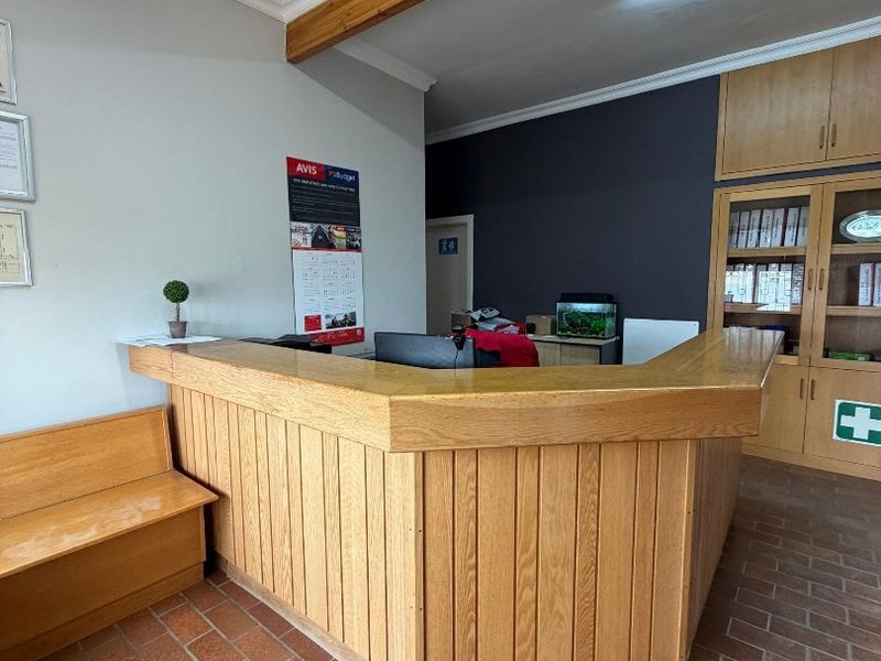 A functional reception area featuring a built-in wooden desk, integrated cabinetry, and durable brick flooring with an exposed wooden ceiling beam.