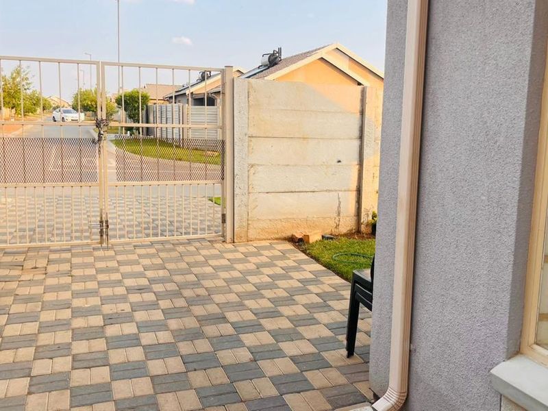 Front entrance area featuring a paved driveway, metal security gate, and precast concrete boundary wall.