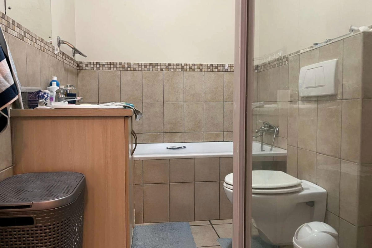 A functional bathroom featuring a built-in bathtub, wall-mounted toilet, and a vanity cabinet with tiled walls and flooring.