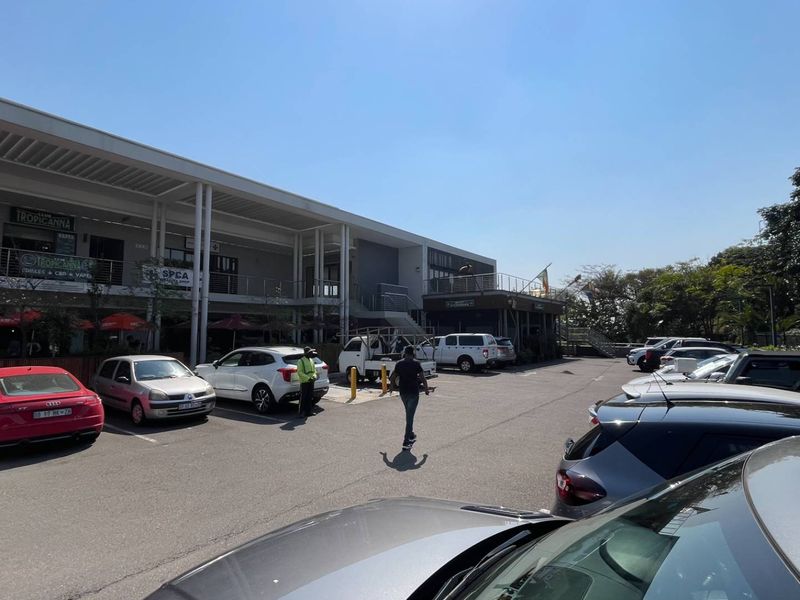 Exterior view of a commercial retail center featuring a paved parking lot, covered walkways, and multiple storefront units.
