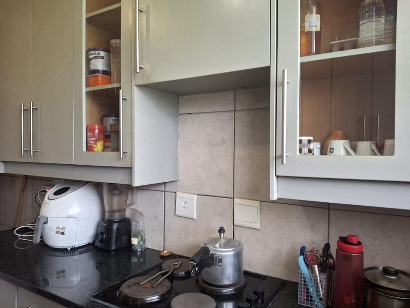 A functional kitchen area featuring built-in cabinetry with glass-fronted doors, a dark granite countertop, and a tiled backsplash with an integrated electric hob.