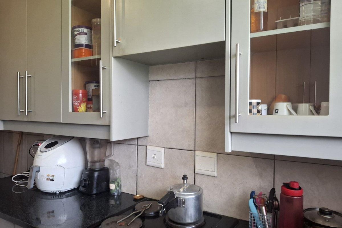 A functional kitchen area featuring built-in cabinetry with glass-fronted doors, a dark granite countertop, and a tiled backsplash with an integrated electric hob.