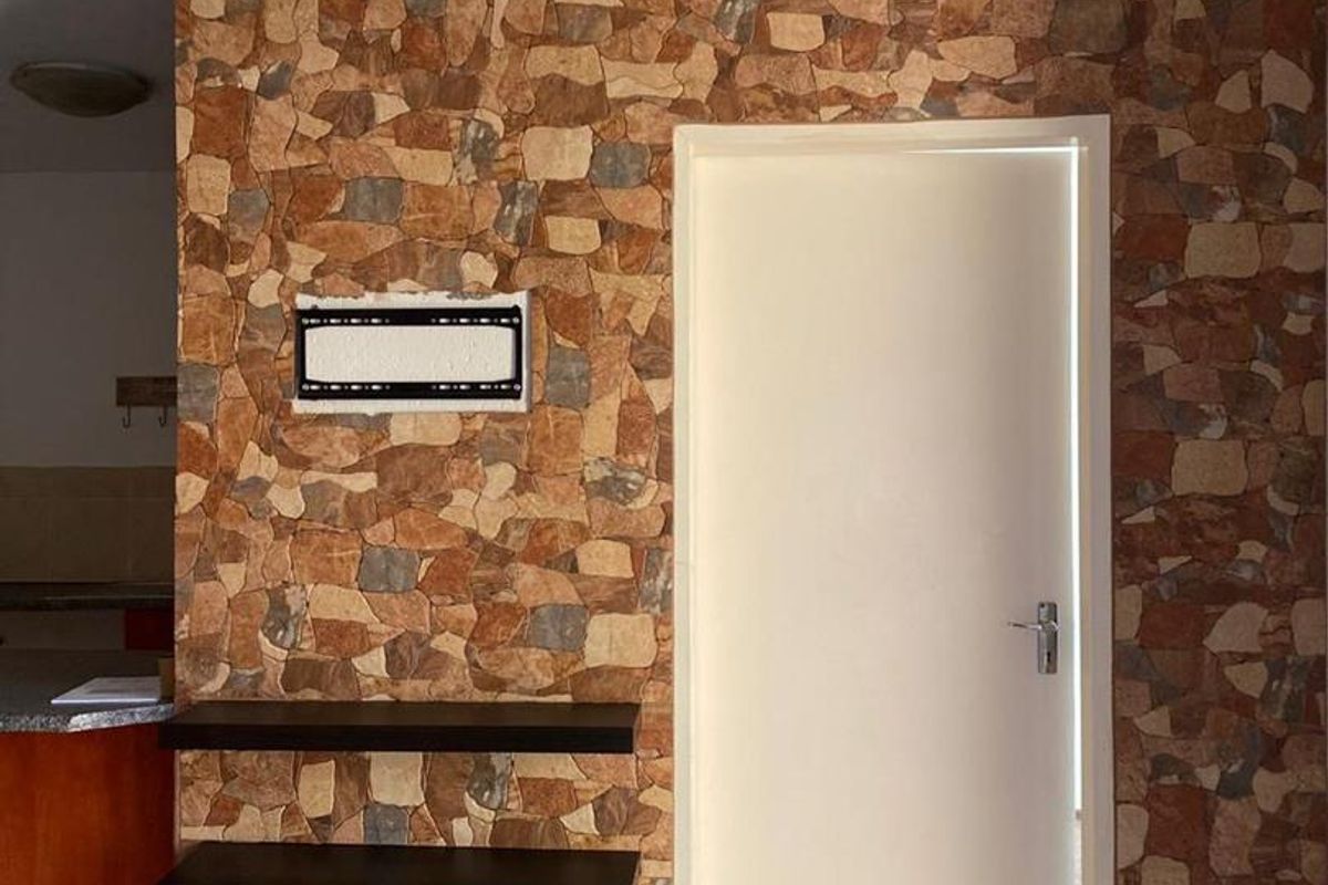 Interior view featuring a stone-clad feature wall with built-in shelving, a standard door, and tiled flooring in an apartment setting.