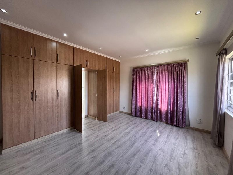 A spacious bedroom featuring extensive built-in wooden cupboards, modern laminate flooring, and recessed ceiling lighting.