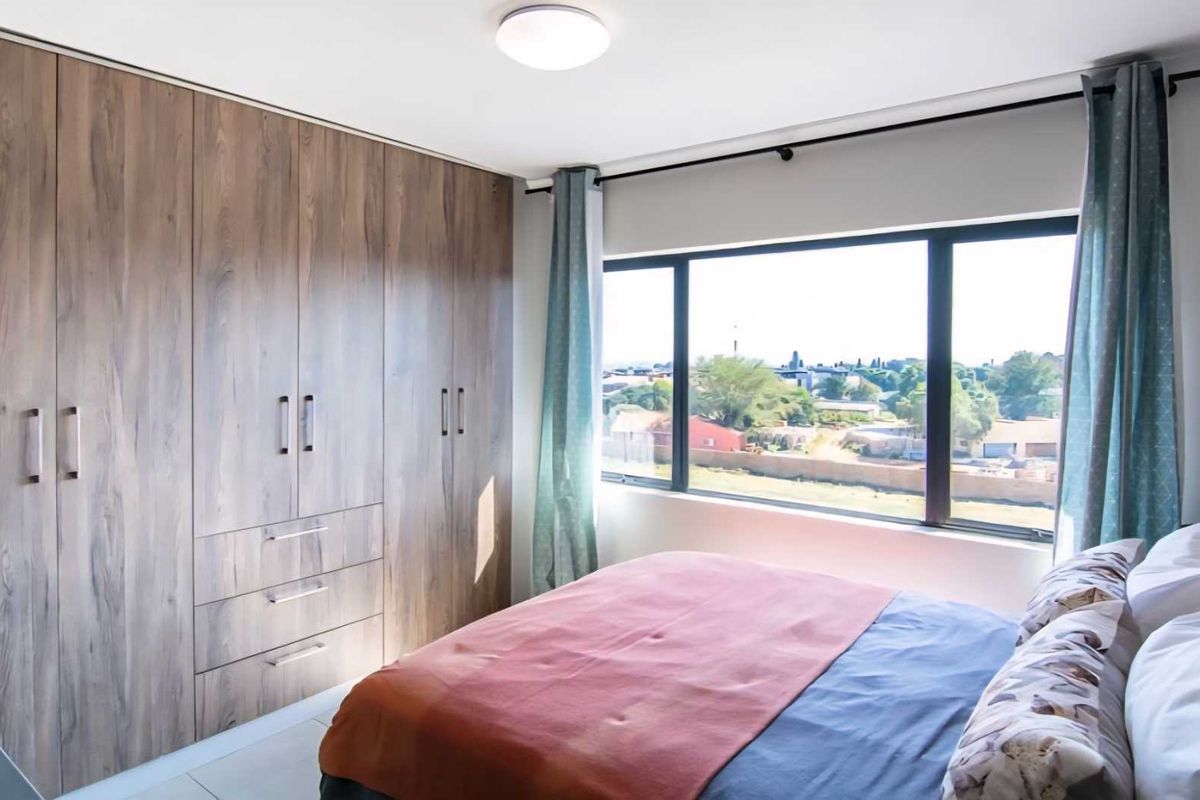 A bright bedroom featuring built-in wooden cabinetry with ample storage and a large window offering natural light and neighborhood views.