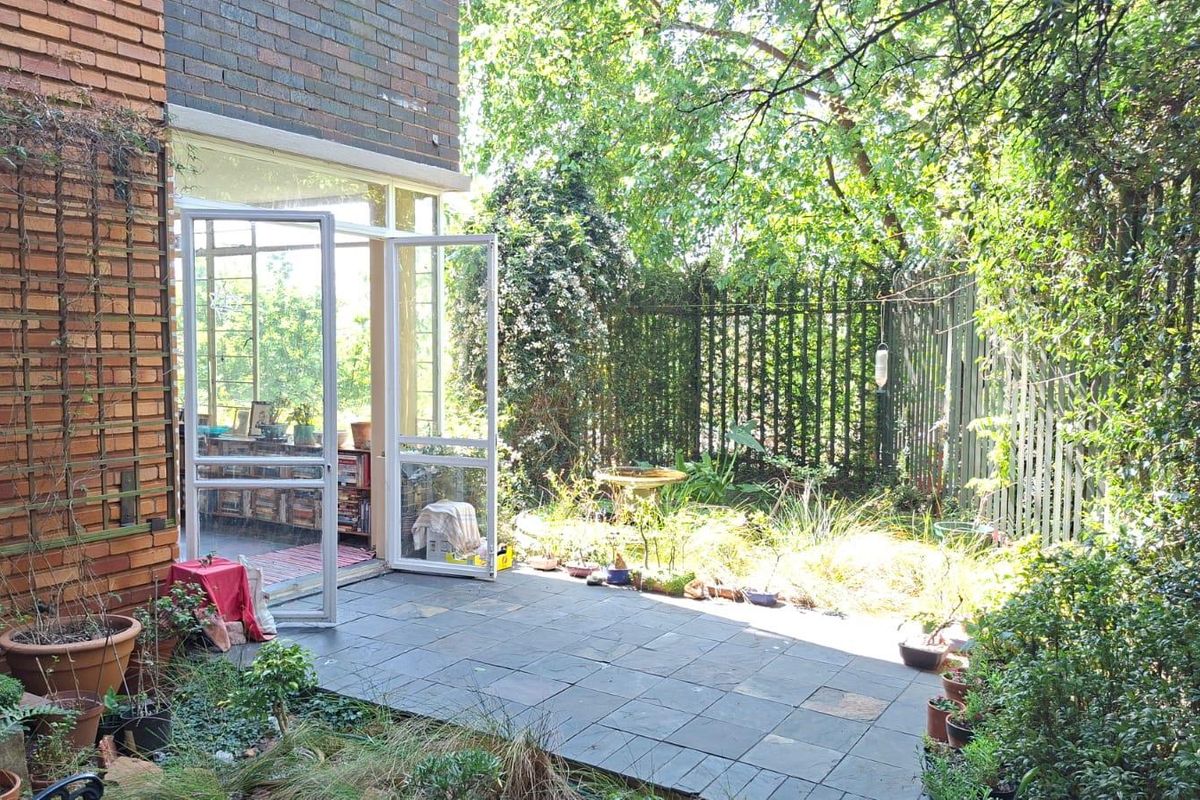 A private rear garden featuring a slate patio area, established greenery, and direct access to the interior through glass double doors.