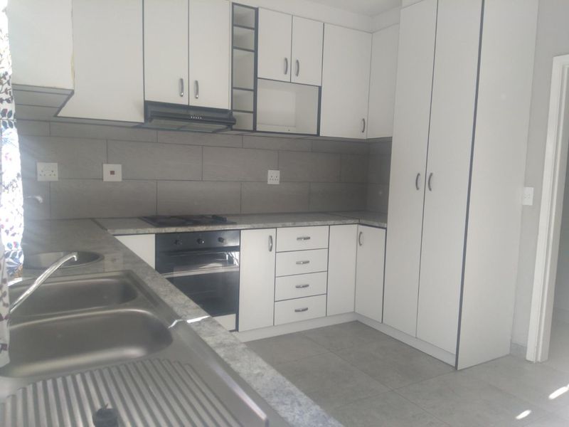 A clean, modern kitchen featuring white cabinetry, grey tiled backsplash, built-in oven, gas hob, and a stainless steel double sink.