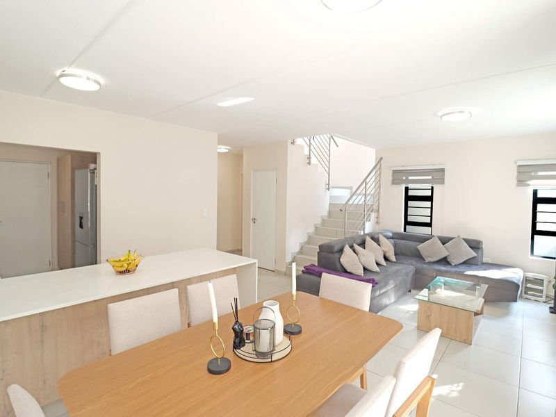 Spacious open-plan living and dining area featuring a modern kitchen island, tiled floors, and a staircase with a contemporary metal balustrade.