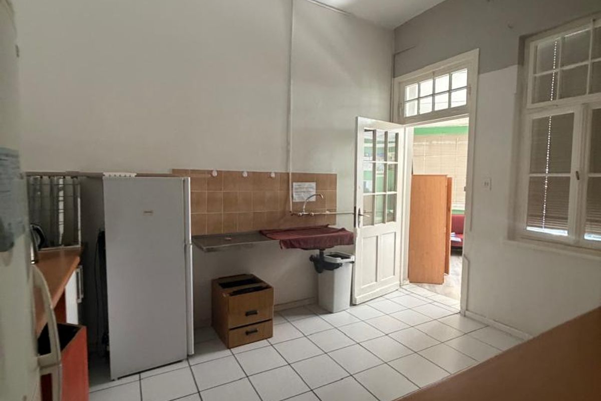 A functional kitchen area featuring tiled flooring, a stainless steel sink with tiled splashback, and direct access to an adjoining room.
