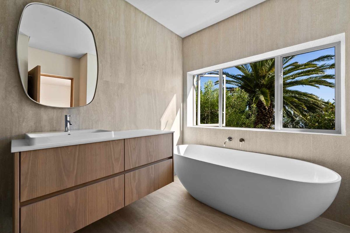 Modern bathroom featuring a sleek floating vanity, integrated sink, and a contemporary freestanding bathtub with views of the garden.