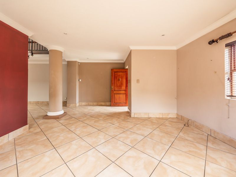 A spacious, empty living area featuring neutral tiled flooring, a prominent structural column, and a wooden entrance door, offering a blank canvas for interior design.