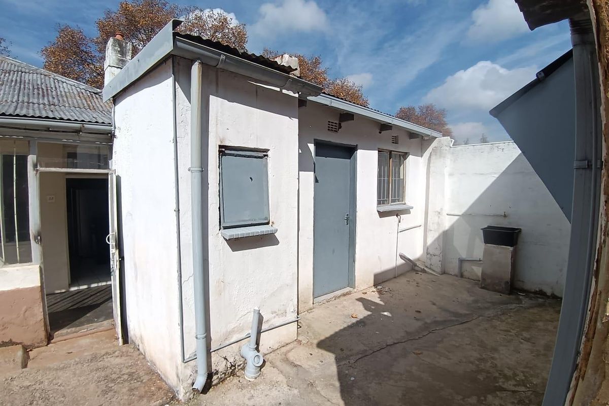 A rear exterior view of the property showing a concrete courtyard area, utility access, and weathered building facade.
