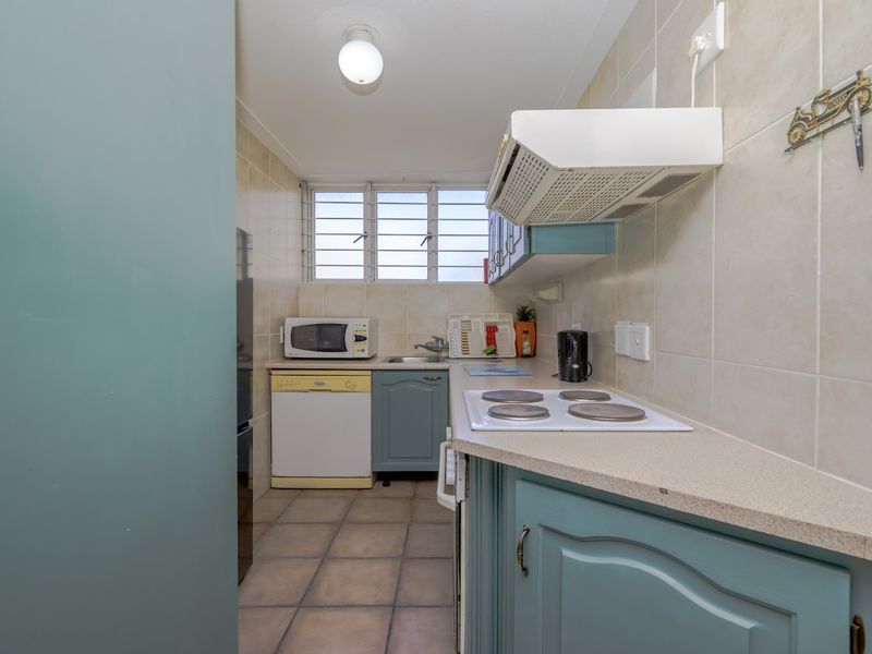 A compact kitchen featuring blue cabinetry, tiled backsplash, electric hob with extractor fan, and tiled flooring.