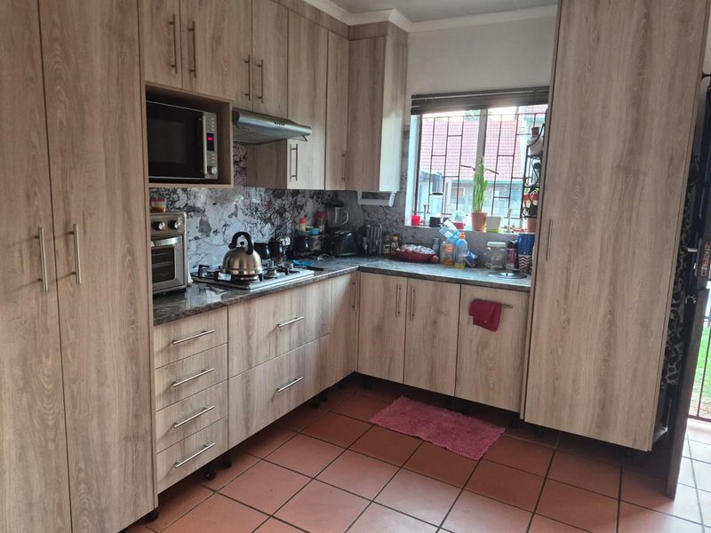A functional kitchen featuring wood-look laminate cabinetry, granite countertops, a gas hob with extractor fan, and tiled flooring.