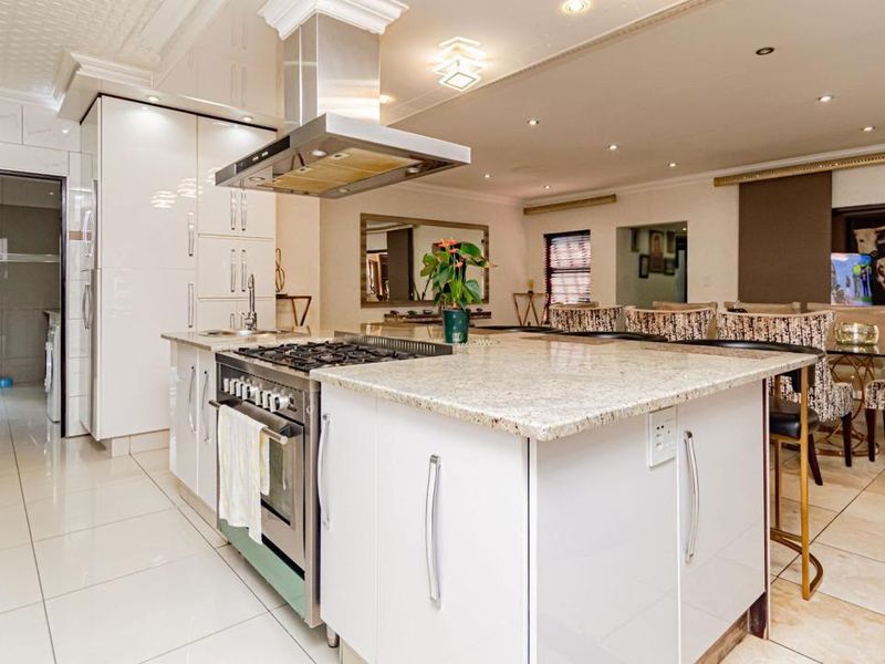 Spacious open-plan kitchen featuring a large island with granite countertops, stainless steel gas stove, extractor fan, and modern glossy cabinetry.