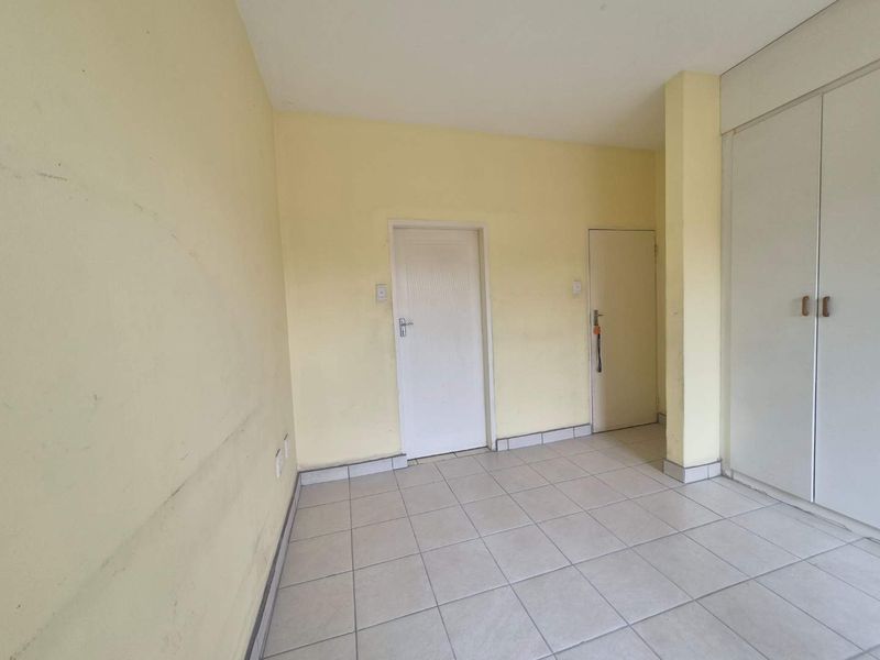 An empty bedroom featuring tiled flooring and built-in cupboards, requiring cosmetic updates to the wall finishes.