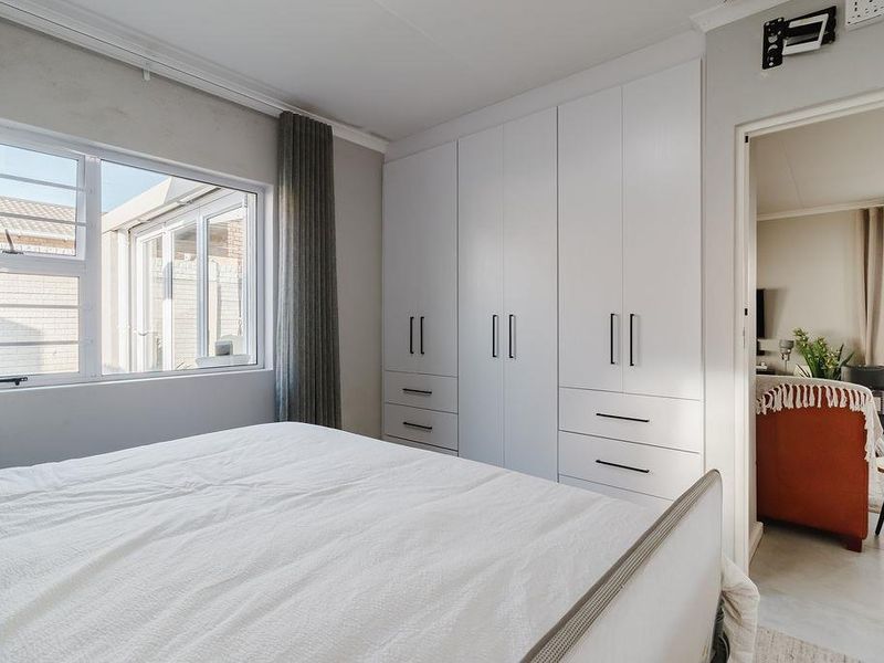 A bright bedroom featuring modern white built-in cupboards, tiled flooring, and aluminium window frames with security bars, offering a clean and functional living space.