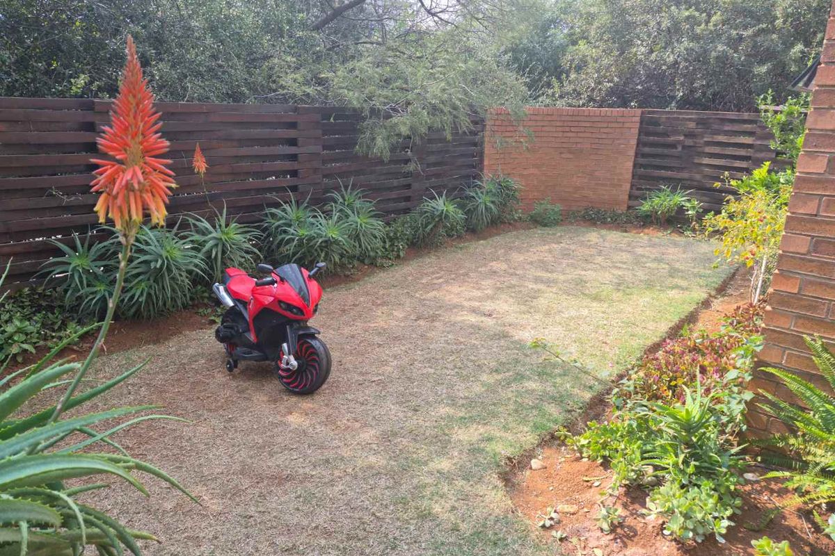 A private rear garden area featuring a brick wall, timber slat fencing, and established garden beds with aloe plants.